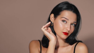 Kalın kırmızı rujlu, siyah saçlı zarif bir kadın şık bir portrede güven içinde poz veriyor. Modelin parlak cildi ve şık görünüşü bu görüntüyü güzellik, moda veya kozmetik için ideal kılar.
