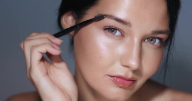 Güzel bir kadın kaşlarını fırçayla mükemmelleştiriyor, yakın plan çekimde makyaj yapıyor. Güzellik dersleri, kozmetik promosyonlar ve cilt bakımı reklamları için ideal. Yüksek kaliteli görüntüler