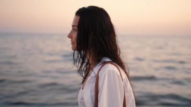 Gün batımında plajda duran bir kadın, arkasında okyanusla nazikçe gülümsüyor. Mutluluk, sükunet ve sakin plaj anları için mükemmel bir tema.. 
