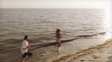 Bir İHA videosu sahilde bir kızın peşinden koşan, sarılıp oynaşan bir adamı gösteriyor. Romantik seyahat reklamları, yaşam tarzı kampanyaları ve tatil promosyonları için ideal.. 