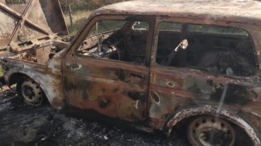 Açık alanda bırakılmış paslanmış, yanmış bir araba enkazının yakın çekim görüntüleri ciddi yangın hasarı gösteriyor. Kazalar, terk edilme, yıkım veya çevresel etki ile ilgili konular için ideal.