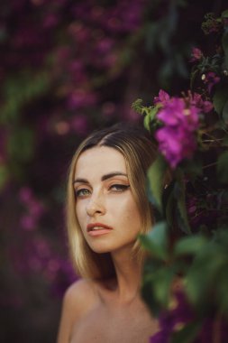 Çekici gözleri olan güzel bir sarışının, canlı mor çiçeklerin arasında zarif bir pozu. Bu kaliteli fotoğraf güzellik, doğa ve yaşam tarzı kavramları için mükemmeldir..