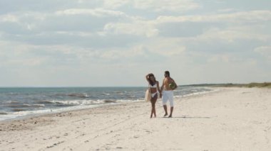 Romantik bir çift, parlak bir gökyüzünün altında sakin bir kumsal boyunca karpuz taşıyan bir adamla el ele dolaşır. Yaz temaları, aşk ve manzaralı kaçamaklar için mükemmel.. 