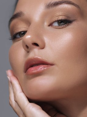 Yüzüne nazikçe dokunan, parlak, pürüzsüz cildini ve parlak dudaklarını vurgulayan bir kadının yakın çekimi. Güzellik, cilt bakımı, kozmetik promosyonlar veya ürün reklamları için mükemmel..
