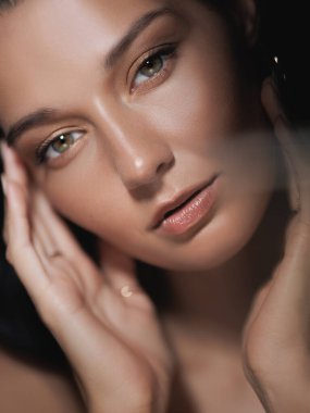 Kusursuz derisi ve yumuşak makyajı olan, yüzüne nazikçe dokunan güzel bir kadının yakın plan portresi. Güzellik, cilt bakımı ve kozmetik ürünler için mükemmel promosyon veya yaşam tarzı içeriği.
