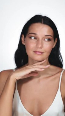 Kusursuz derisi olan güzel bir kadın yakın plan portrede nazikçe çenesine dokunuyor. Güzellik, cilt bakımı ve doğal ışıltı ve sağlıklı cilt üzerine odaklanmış kozmetik reklamlar için mükemmel..