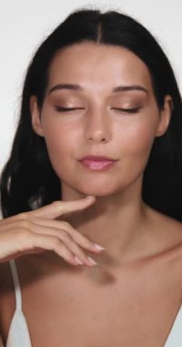 Kusursuz derisi olan zarif bir kadının yakın plan portresi, düzgün bir duruşla çenesine hafifçe dokunuyor. Güzellik reklamları, cilt bakımı promosyonları ve parıldayan, ışıl ışıl parlayan kozmetik kampanyaları için ideal.