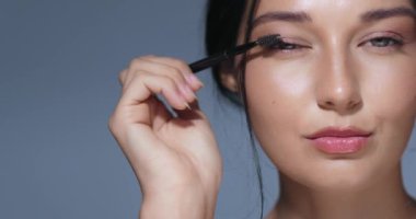 Parlak tenli ve doğal makyajlı güzel bir kadın stüdyo ortamında kirpiklerini fırçayla tarıyor. Güzellik dersleri, kozmetik promosyonları ve cilt bakımı için mükemmel.. 