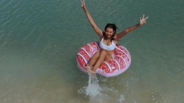 Beyaz bikinili neşeli bir kadın süper yavaş çekimde kristal berrak tropikal sulara atlıyor, pembe donut şeklinde şişme bir suya iniyor. Yaz ve plaj görselleri için mükemmel.. 