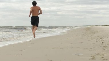 Hava bulutluyken ıssız bir plaj boyunca koşan bir adam fitness, yalnızlık ve doğanın saf güzelliğini vurgular. Bu resim kavramsal ve promosyon projeleri için mükemmel.. 