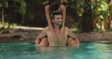 Bereketli yeşilliklerle çevrili, tropik bir havuzda kucaklaşan neşeli bir çift. Bu yüksek kaliteli stok videosu aşk, sükunet ve tatil temalarını yakalamak için idealdir.