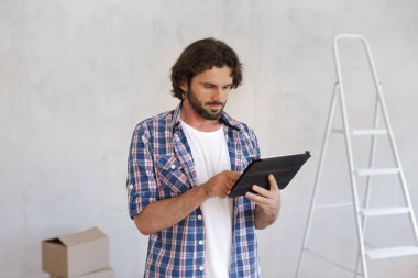 Ekose gömlekli bir adam DIY ev yenileme projesi planlamak için tablet kullanıyor. Ev geliştirmesi, iç tasarım ve proje yönetimi ile ilgili kavramlar için ideal. 