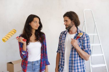Ciddi bir çift, günlük giysiler içinde ellerinde boya silindiri ve fırçayla DIY ev yenileme projesini tartışıyorlar. Ev yenileme, iç tasarım ve proje planlama kavramları için mükemmel.. 
