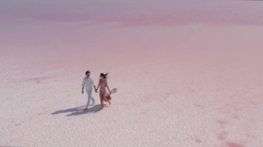 Parlak bir gökyüzünün altında, engin pembe bir tuz gölü boyunca el ele yürüyen bir çiftin güzel hava manzarası. Romantik, seyahat ve doğa temalı projeler için mükemmel.. 