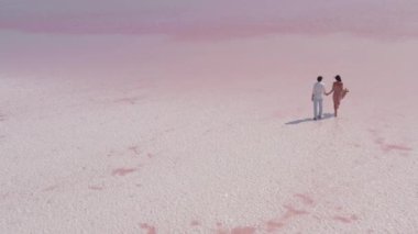 Serin pembe tuz gölünde el ele yürüyen bir çiftin nefes kesici hava görüntüsü. Romantik, seyahat ya da minimalist güzellikte doğa temalı görseller için idealdir.. 