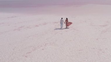 Bir çiftin el ele tutuşup uçsuz bucaksız pembe bir tuz gölünde berrak bir gökyüzünün altında yürürken çekilmiş romantik bir fotoğrafı. Aşk, seyahat ve doğa temalı görseller için mükemmel.. 