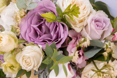 Lavanta, beyaz ve soluk sarı güller içeren, yemyeşil ve kurdelelerle süslenmiş karışık çiçek buketinin zarif yakın çekimi. Düğün temaları, romantik hediyeler ve çiçek aranjmanları için ideal.. 