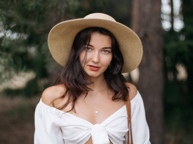 Beyaz bir bluz ve hasır şapka giyen güzel bir kadın doğal ortamın tadını çıkarıyor. Bu yüksek kaliteli görüntü yaşam tarzı, moda ve doğa temalı içerik için mükemmeldir, zarafeti yakalar.