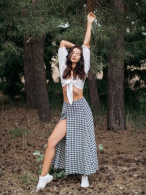 Beyaz bir bluz ve kareli etek giyen şehvetli bir kadın ormanda zarif bir poz veriyor. Bu yüksek kaliteli görüntü moda, yaşam tarzı ve doğa temalı içerik için idealdir, zarafeti yakalar.