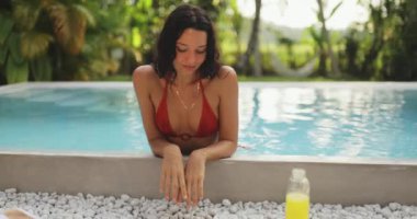 Sonsuzluk havuzunun kenarına yaslanmış, arka planda yemyeşil bir hava olan zarif bir kadın. Tatilleri, refahı, tropikal inzivaları ve lüks yaşamı desteklemek için idealdir.. 