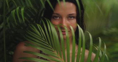 Bereketli tropikal yaprakların arasından bakan güzel bir kadının yakın çekimi büyüleyici bakışları ve canlı yeşillikle kusursuz bir şekilde harmanlanan doğal güzelliği. Egzotik ve şehvetli konular için mükemmel.. 