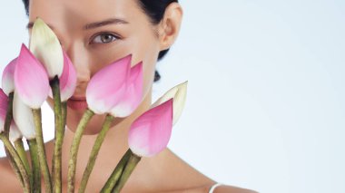 Pembe nilüfer çiçeklerinin arkasına kısmen saklanan genç bir kadının, sakin ve minimalist bir güzellik konsepti yaratması. Doğal görünüş ve yumuşak renkler saflığı, sağlığı ve zarafeti çağrıştırıyor..