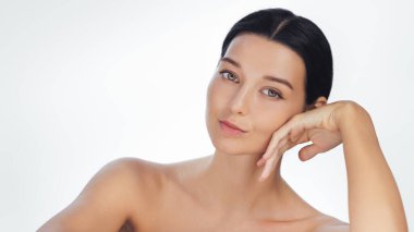 Çıplak omuzlu sakin bir genç kadın, eli çenesinde, kusursuz cildini ve doğal güzelliğini ön plana çıkarıyor. Bu yüksek kaliteli görüntü cilt bakımına, güzelliğe veya sağlığa uygundur.