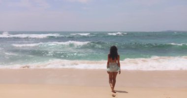 Bikinili bir kadının kumlu bir plajda, kolları açık, okyanus dalgalarına bakan görüntüsü. Tatil, seyahat, özgürlük ve yaz yaşam tarzı kavramları için mükemmel.. 