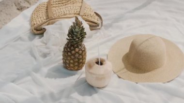 El yapımı bir çadır, taze ananas, hindistan cevizi içeceği, hasır şapka ve yumuşak beyaz bir battaniyeye örülmüş örgü içeren tropikal bir plaj ortamının yavaş çekim görüntüleri. Yaz görselleri için ideal. 