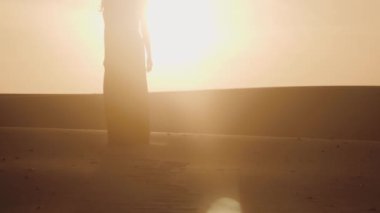 Çöl günbatımının altın parıltısına karşı dalgalı bir elbise giymiş nefes kesici bir kadın silueti. Sahne, yumuşak ışıkta güzellik, huzur ve sonsuz zarafeti yakalar..