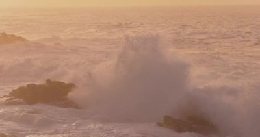 Okyanus dalgalarının gün batımında kayalık araziye çarptığı destansı yavaş çekim videosu. Dramatik sıçramalar ve altın sis büyüleyici ve nefes kesici bir doğal manzara yaratır..