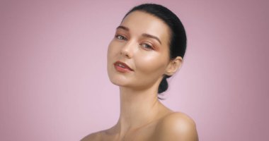 Göz kamaştırıcı esmer kadın, parlak akşam makyajıyla, yumuşak pembe arka planda poz veriyor. Yüksek kaliteli reklamlarda güzellik, makyaj ve cilt ürünlerini tanıtmak için mükemmel..