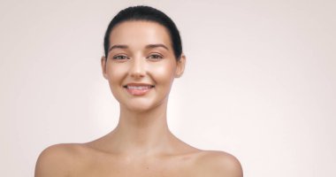 Pembe bir arka plana gülümseyen parlak, parlak tenli beyaz bir kadının yakın plan portresi. Güzellik, cilt bakımı ve sağlık konuları için mükemmel. Yüksek kaliteli resim için uygun