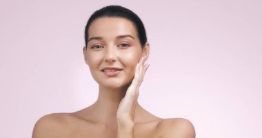 Yüzüne hafifçe dokunan ve gülümseyen beyaz tenli genç bir kadının yakın plan portresi. Güzellik, cilt bakımı ve sağlık konuları için mükemmel. Yüksek kaliteli resim