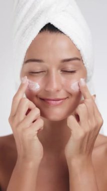 Havlu türbanlı neşeli kadın yanaklarına nazikçe cilt kremi sürüyor, doğal güzellik yayıyor. Güzellik, kendine bakım ya da cilt bakım ürünleri promosyonları için mükemmel. 