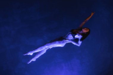 A woman floats gracefully in a swimming pool at night, illuminated by calming blue light. This serene and atmospheric image is perfect for concepts of relaxation, beauty, and nighttime escape. clipart