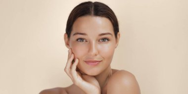 Yüzüne hafifçe dokunan ışıl ışıl cildi olan bir kadının yakın plan portresi. Kusursuz teni ve pürüzsüz teni bu görüntüyü güzellik, makyaj ve cilt tanıtımı için mükemmel kılıyor.