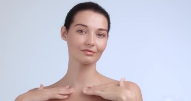 Işıl ışıl cildi ve yumuşak bir gülümsemesi olan, köprücük kemiğine hafifçe dokunan kendinden emin bir kadının portresi. Cilt bakımı kampanyaları, güzellik reklamları ve lüks sağlık promosyonları için ideal.. 