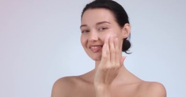 Çıplak makyajlı ışıl ışıl bir kadın yüzüne nazikçe cilt losyonu sürüyor. Güzelliği ve rahatlığı somutlaştırıyor. Güzellik, kaplıca ve cilt bakımı için mükemmel. Yüksek kaliteli görüntüler ve ideal