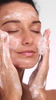 Gülümseyen bir kadının yüzünü köpüklü bir yüz temizleyiciyle temizlerken. Temiz ve sağlıklı cilde odaklanan cilt bakımını, güzelliği veya sağlık ürünlerini teşvik etmek için mükemmel.. 