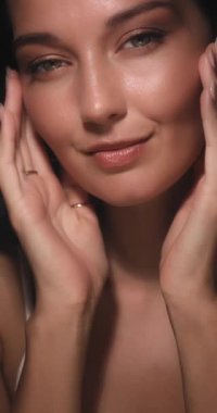 Parlak altın makyajlı ve kusursuz parlak tenli elleri çerçeveli zarif poz veren bir kadının yakın çekimi. Güzellik, cilt bakımı ve kozmetik promosyonları için ideal.. 