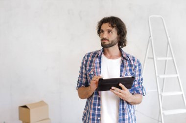 Elinde tablet olan düşünceli bir adam, bir ev yenileme projesi planlıyor. DIY, ev geliştirmesi, iç tasarım ve proje yönetimi ile ilgili kavramlar için ideal. 