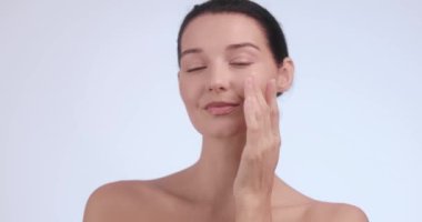 Minimalist bir stüdyoda yüzüne nemlendirici krem sürerken ışıl ışıl cildi olan güzel bir kadın hafifçe gülümsüyor. Güzellik, cilt bakımı ve kozmetik reklamları için ideal.. 