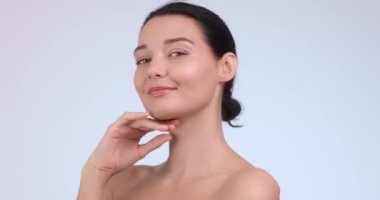 Yüzüne hafifçe dokunarak gülümseyen parlak tenli genç bir kadının yakın çekimi. Cilt bakımı kavramları, güzellik ürünleri tanıtımı ve kişisel bakım kampanyaları için mükemmel.. 