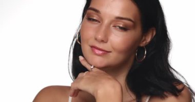 Parlak bir stüdyoda kendine güveni olan, altın rengi makyajlı ve parlak tenli bir kadın zarif bir poz veriyor. Güzellik, kozmetik, moda ve akşam makyajı için ideal promosyon içeriği. 