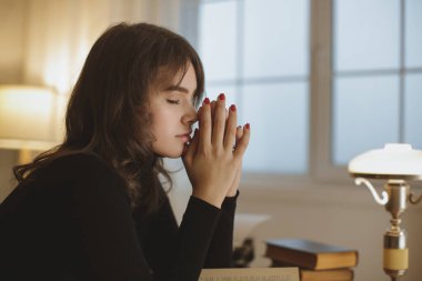 Siyah bluzlu, elleri yüzü ve gözleri kapalı genç bir kadın, kitaplarla dolu bir masanın yanında oturuyor ve sıcak, rahat bir çalışma odasında parlayan bir lamba. İç gözlem ya da yaşam tarzı için mükemmel