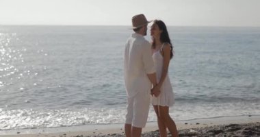 Neşeli bir çift kumsalda romantik bir yürüyüş yapar, el ele tutuşur ve güler. Sakin okyanus, yumuşak kum ve doğal kaya oluşumları aşk ve mutluluk için mükemmel bir zemin oluşturur..