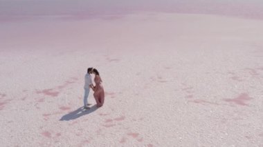 Sakin pembe bir tuz gölünde romantik bir öpücüğü paylaşan bir çiftin nefes kesici hava görüntüsü. Aşk, seyahat, düğün ya da minimalist titreşimli doğa temalı görseller için mükemmel.. 
