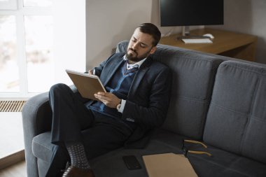 Takım elbiseli profesyonel bir adam kanepede oturuyor, not defterine odaklanmış bir ifadeyle notlar yazıyor. İş, şirket ve yaşam tarzı temalı fotoğrafçılık için mükemmel.. 