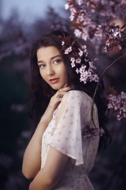 Young woman with a radiant smile and dark flowing hair, standing gracefully among cherry blossoms in soft spring light. Ideal for beauty editorials, romantic themes, and floral photography.  clipart